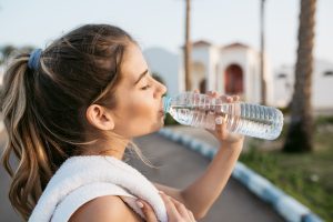 Closeup portrait thirsty young pretty woman drinking water from bottle during training on street in sunny morning. Cheerful mood, chilling with closed eyes, summer, fitness time